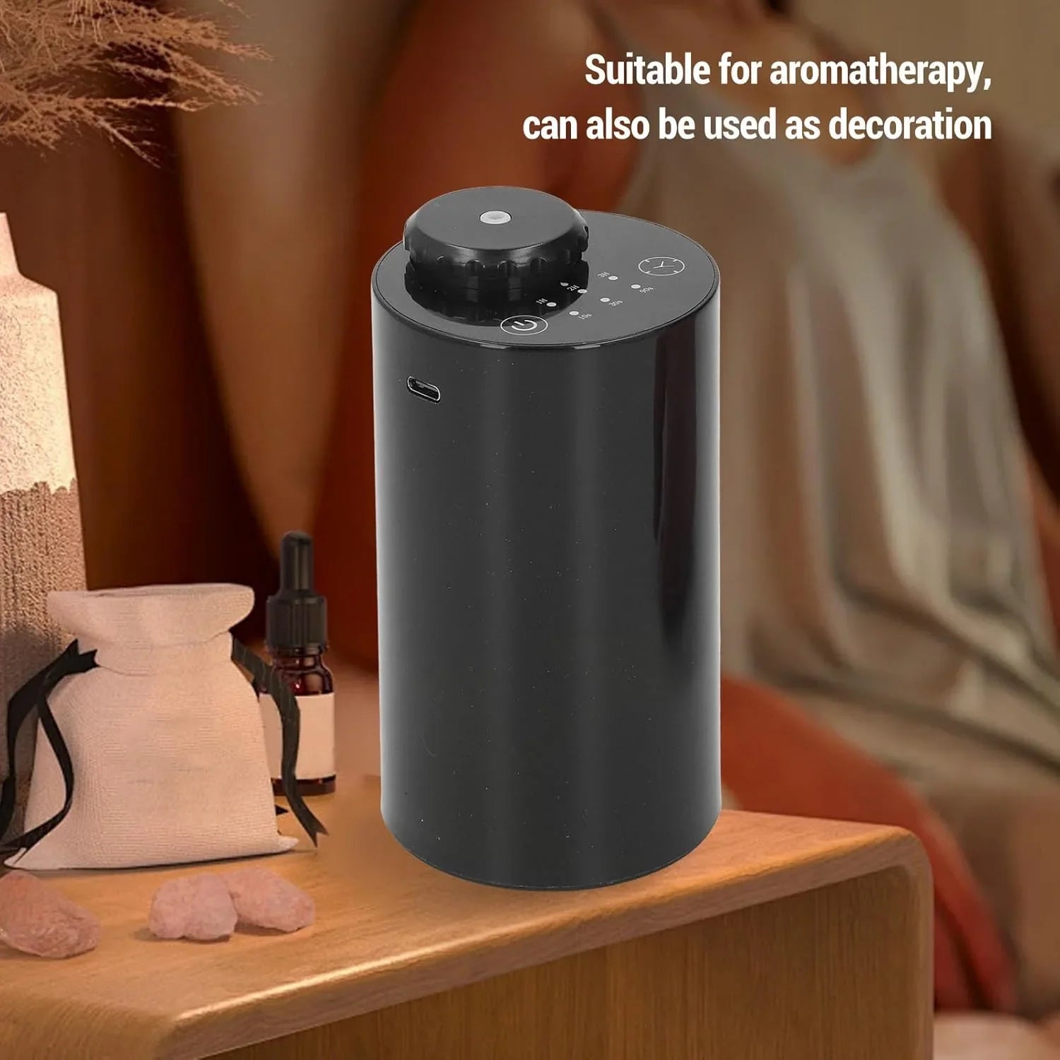 Black cylindrical aromatherapy diffuser on wooden table with essential oil bottle and decorative pouch
