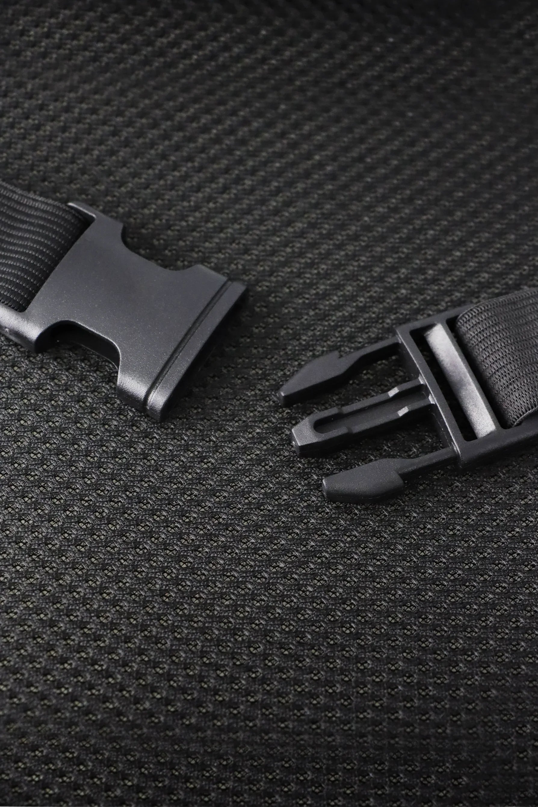 Close-up of black plastic buckle clasp with strap on textured black fabric background