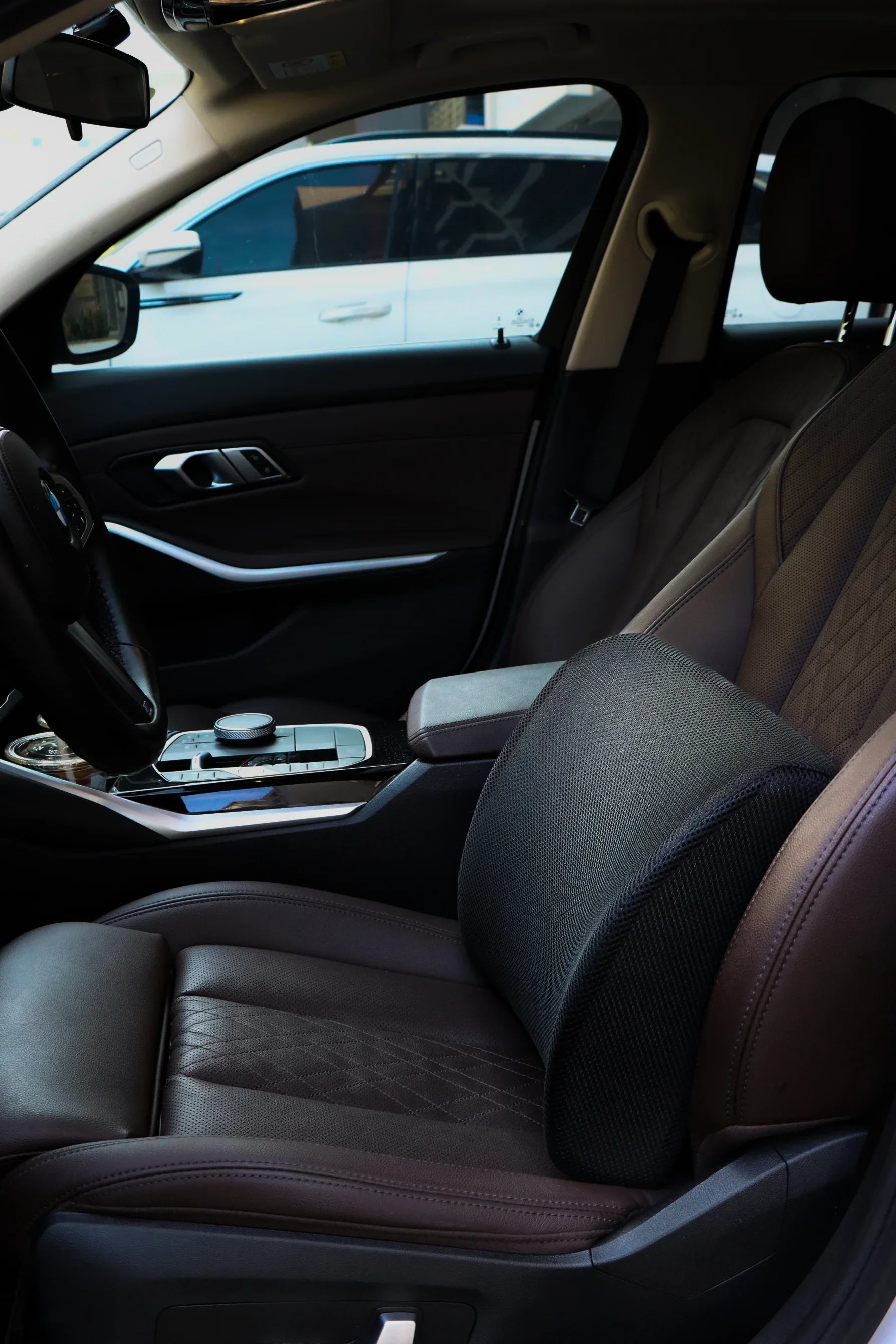 Car interior with brown leather seats and black lumbar support cushion on driver's seat